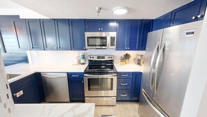 A modern kitchen with stainless steel appliances, blue cabinets, and a marble countertop. - Islander Beach Resort 506 2 Bedroom Condo (Fort Walton Beach)
