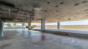 An indoor parking area with concrete pillars, a tiled floor, and a view of a bridge and palm trees outside. - Islander Beach Resort 506 2 Bedroom Condo (Fort Walton Beach)