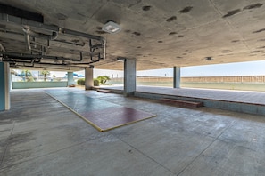 Ein Parkhaus mit Betonpfeilern, Fliesenboden und Blick auf eine Brücke sowie Palmen im Freien.
