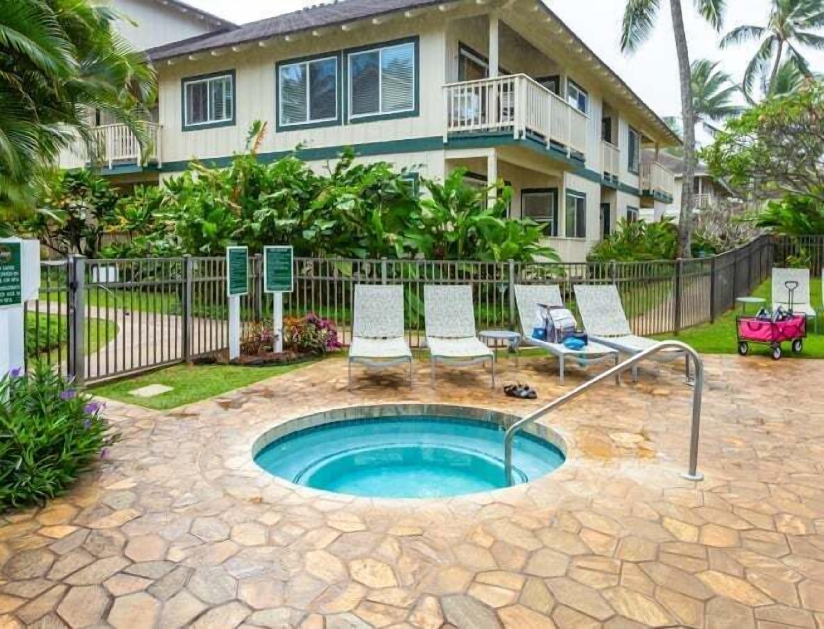 A pool area with lounge chairs, a small pool, and a building with a balcony.