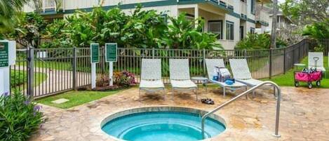 A pool area with lounge chairs, a small pool, and a building with a balcony.