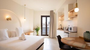Une chambre d’hôtel comprenant un lit, une table à manger avec des chaises, un coin cuisine et une vue sur l’extérieur, visible à travers une porte.