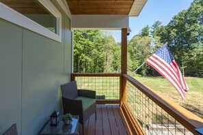 A covered porch with a wicker chair, a small table with a plant, and an American flag. - Murray Creek Hollow - Private Asheville Escape (Asheville)