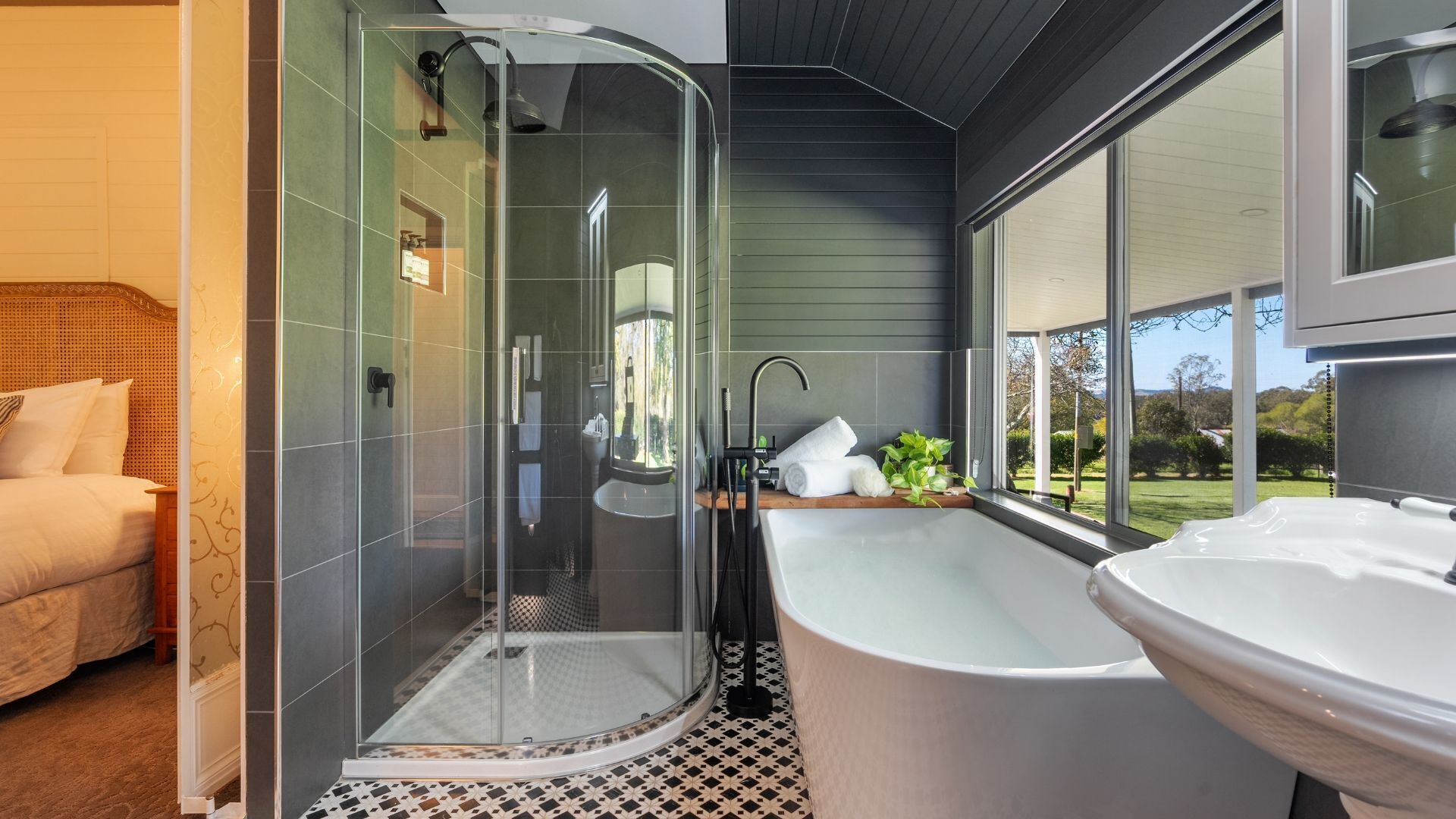 A modern bathroom with a glass-enclosed shower, a freestanding bathtub, and a large window offering a view of the outdoors.