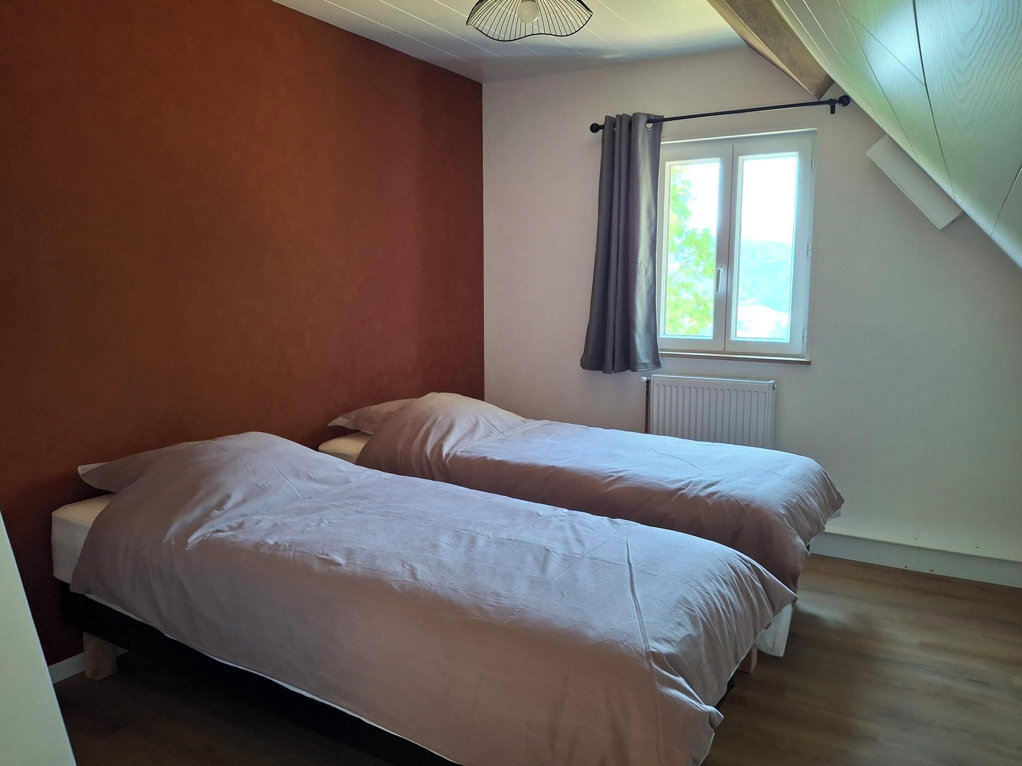 Una habitación con dos camas, una ventana con cortinas, un radiador y techo inclinado.
