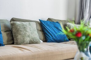 Ein Sofa mit mehreren Kissen in neutralen Farbtönen und ein Blumenstrauß im Vordergrund.