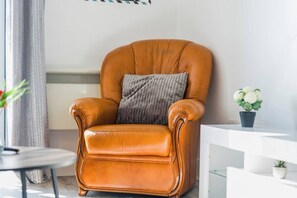 A tan leather armchair with a cushion, positioned in a modern room with a radiator, a small table, and a potted plant. - #130 Free Parking Stylish Apt City Centre|sleeps 6 (West Midlands)