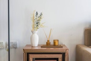 Ein kleiner Holztisch mit einer weißen Vase mit Trockenpflanzen, einer braunen Vase mit Schilfhalmen und einem goldenen Kerzenhalter.
