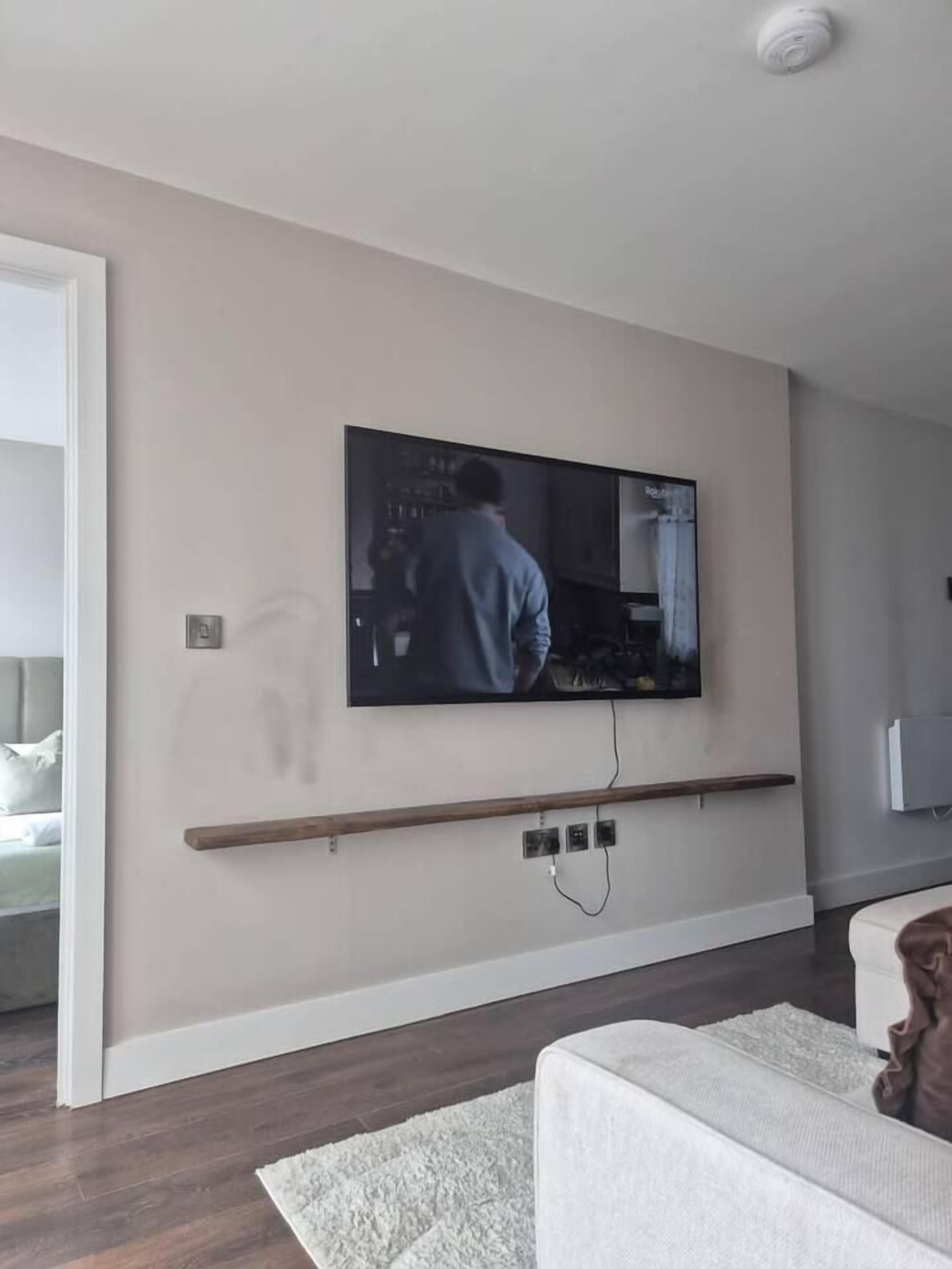 A modern living room with a mounted television, a wooden shelf, and a white sofa.
