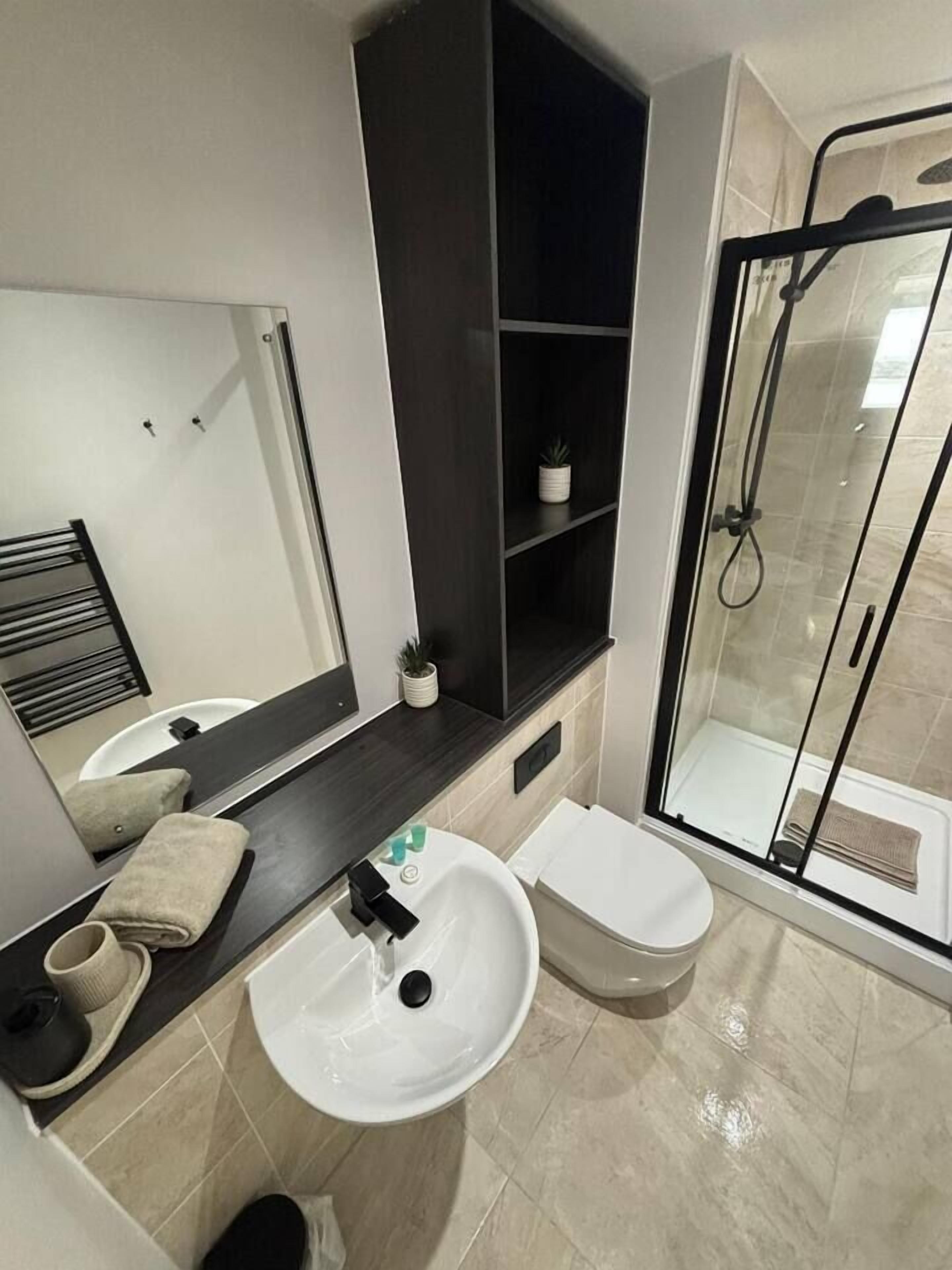 A modern bathroom with a large mirror, a white sink, a toilet, and a glass-enclosed shower.