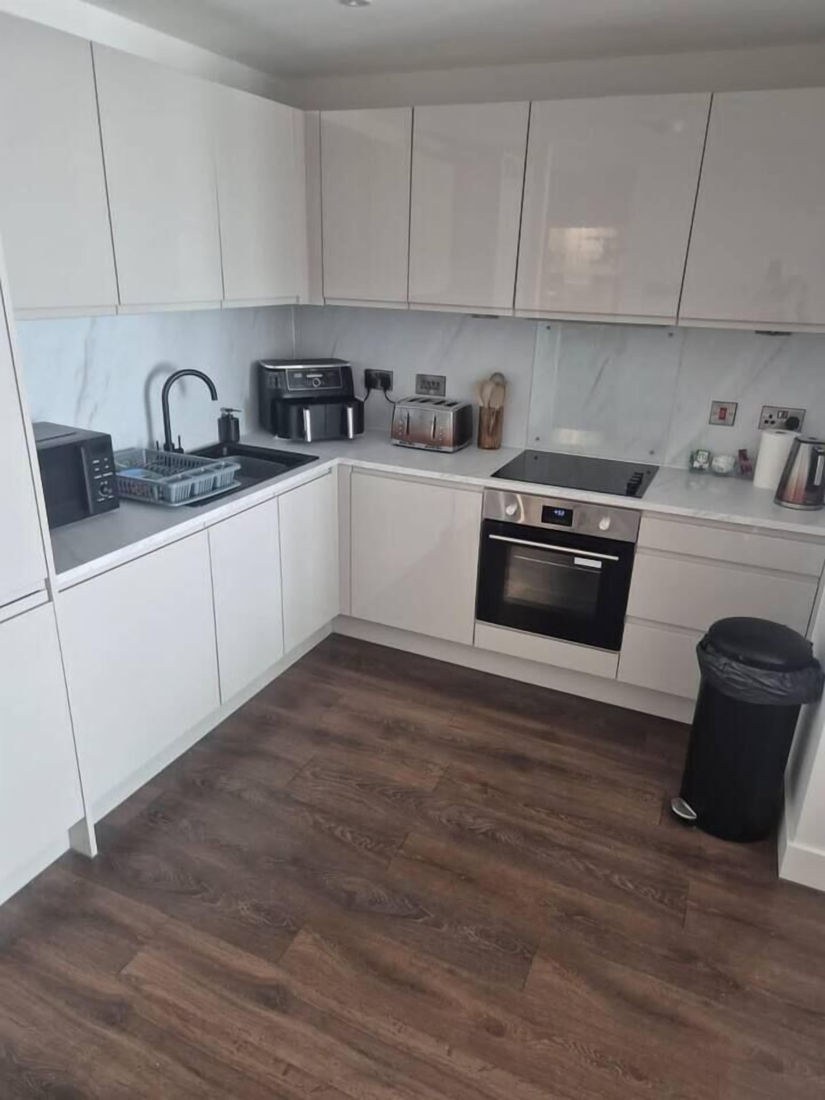 A modern kitchen with white cabinets, a black countertop, a built-in oven, and a coffee machine.