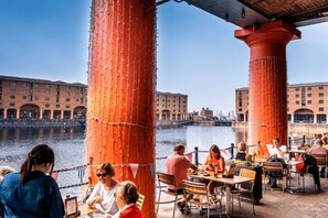 A waterfront restaurant with outdoor seating, red pillars, and a view of historic buildings across the water. - #132 Stylish Luxury Flat | Free Parking |City View (Merseyside)