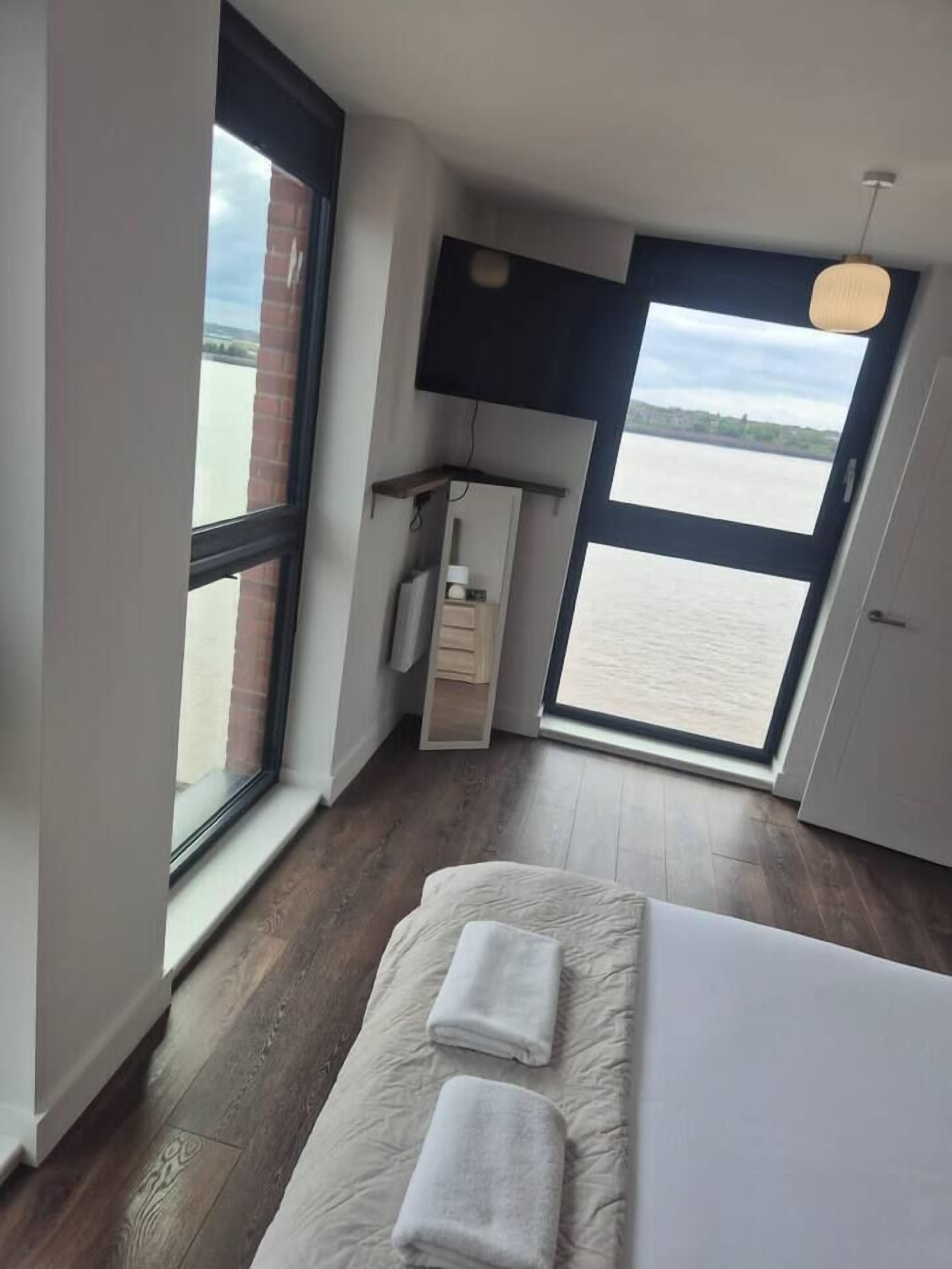 A bedroom with a large window, a bed, a bedside table, and a hanging light fixture.