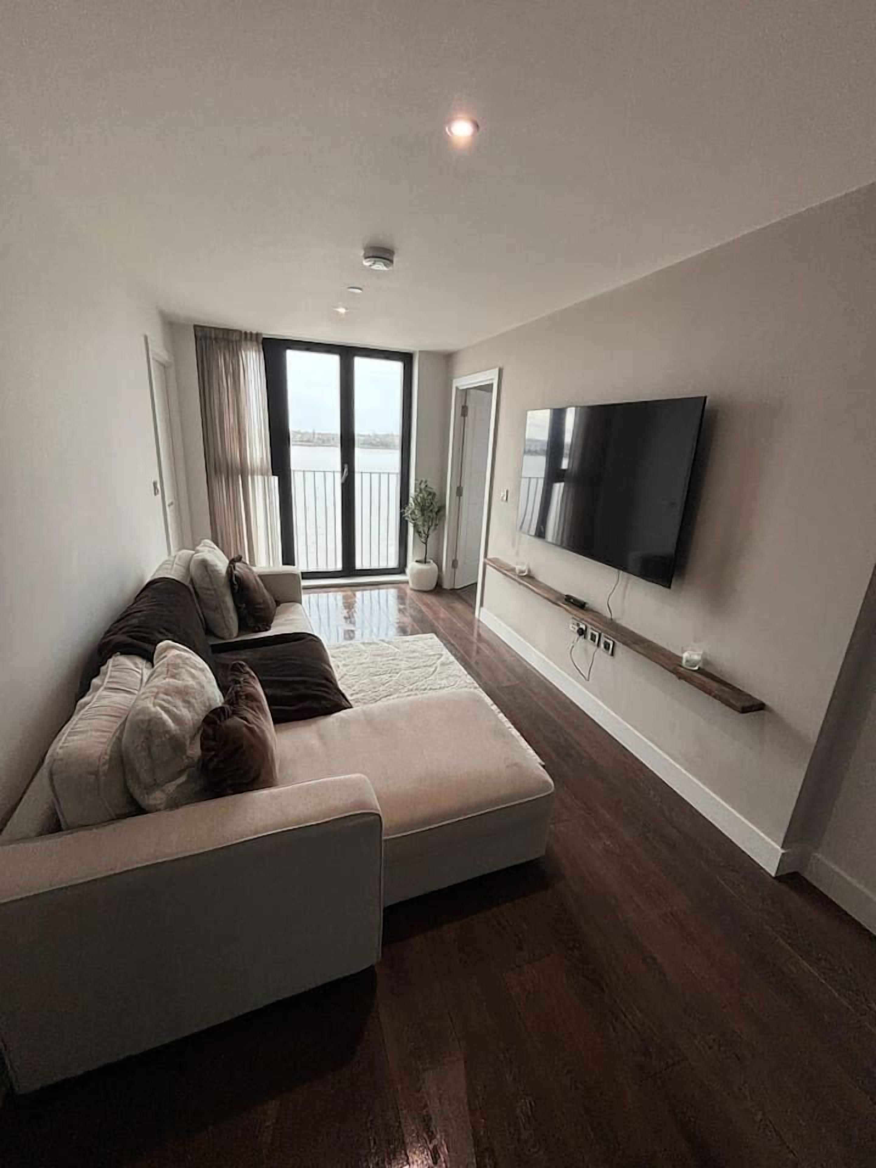 Ein modernes Wohnzimmer mit einer Eckcouch, einem flachbildfernseher an der Wand und einer Glastür zum Balkon.