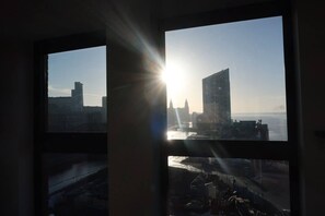 Blick durch ein Fenster: sonnendurchflutete Stadtansicht und ein Gewässer.