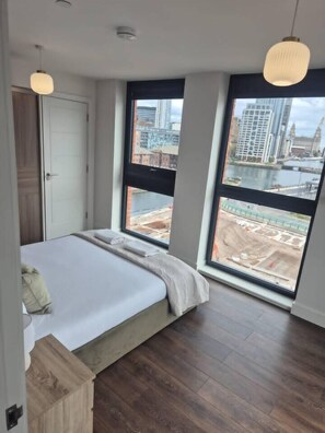 Ein Schlafzimmer mit einem großen Bett, einem Holzkopfende und Blick auf eine Baustelle durch große Fenster.