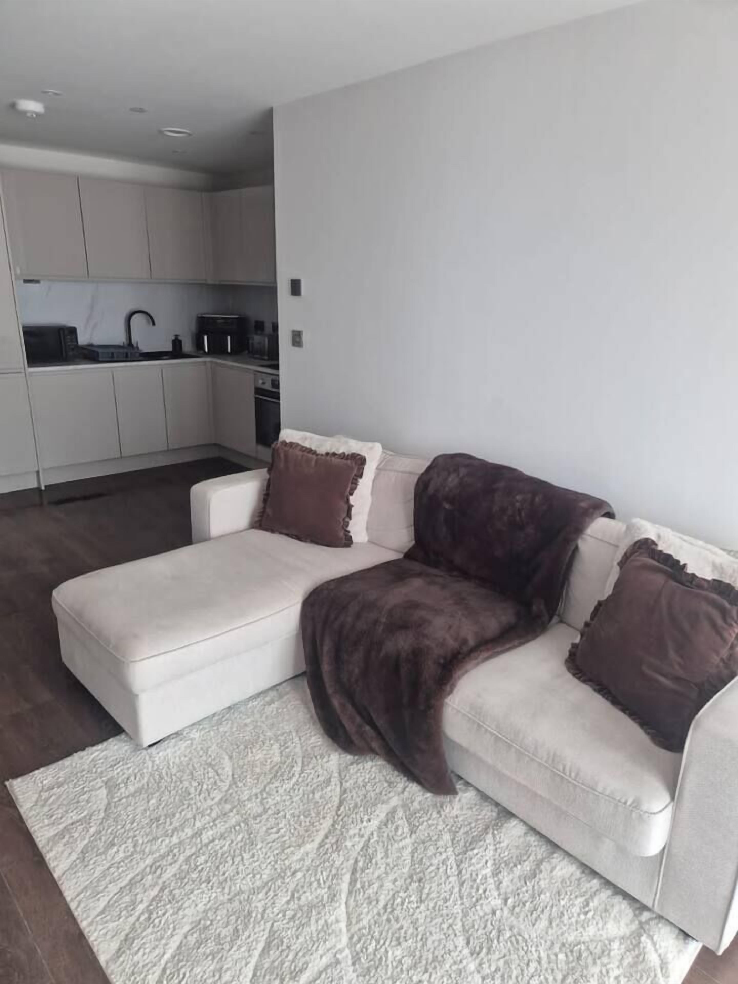 A modern living room with a white sofa, a patterned rug, and a kitchen in the background.