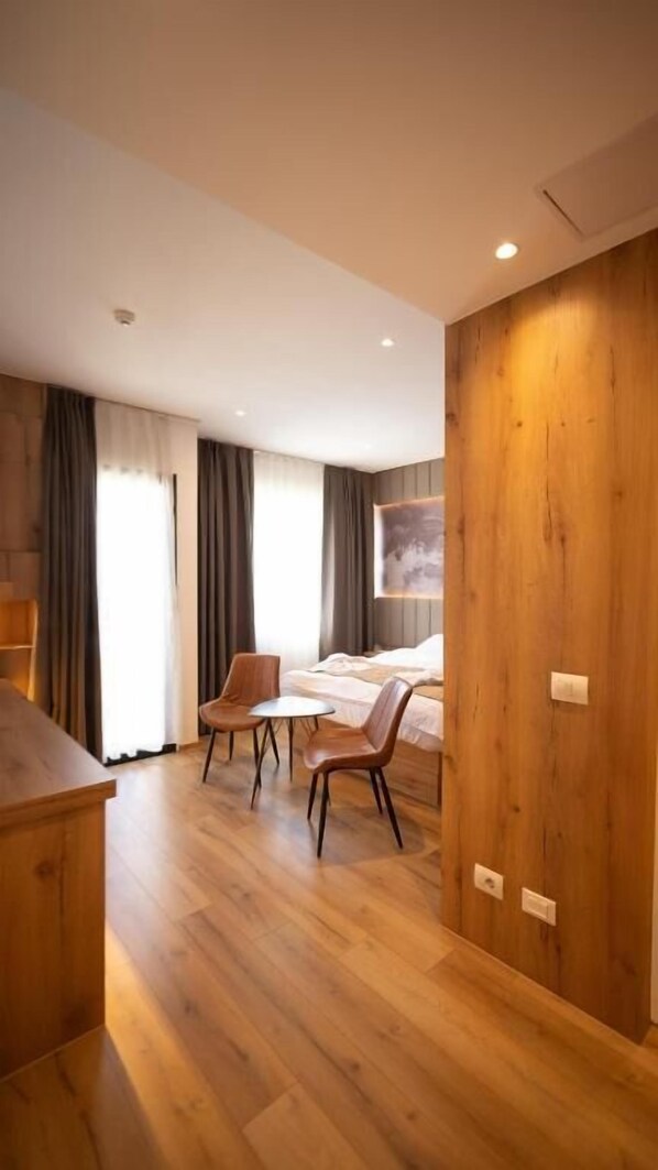 A modern hotel room with a wooden floor, a bed, a desk, and two chairs.