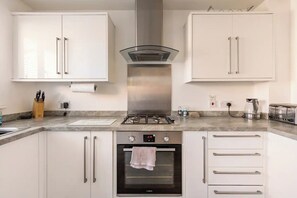 Een moderne keuken met witte kasten, een gasfornuis, een oven en een rvs-afzuigkap.