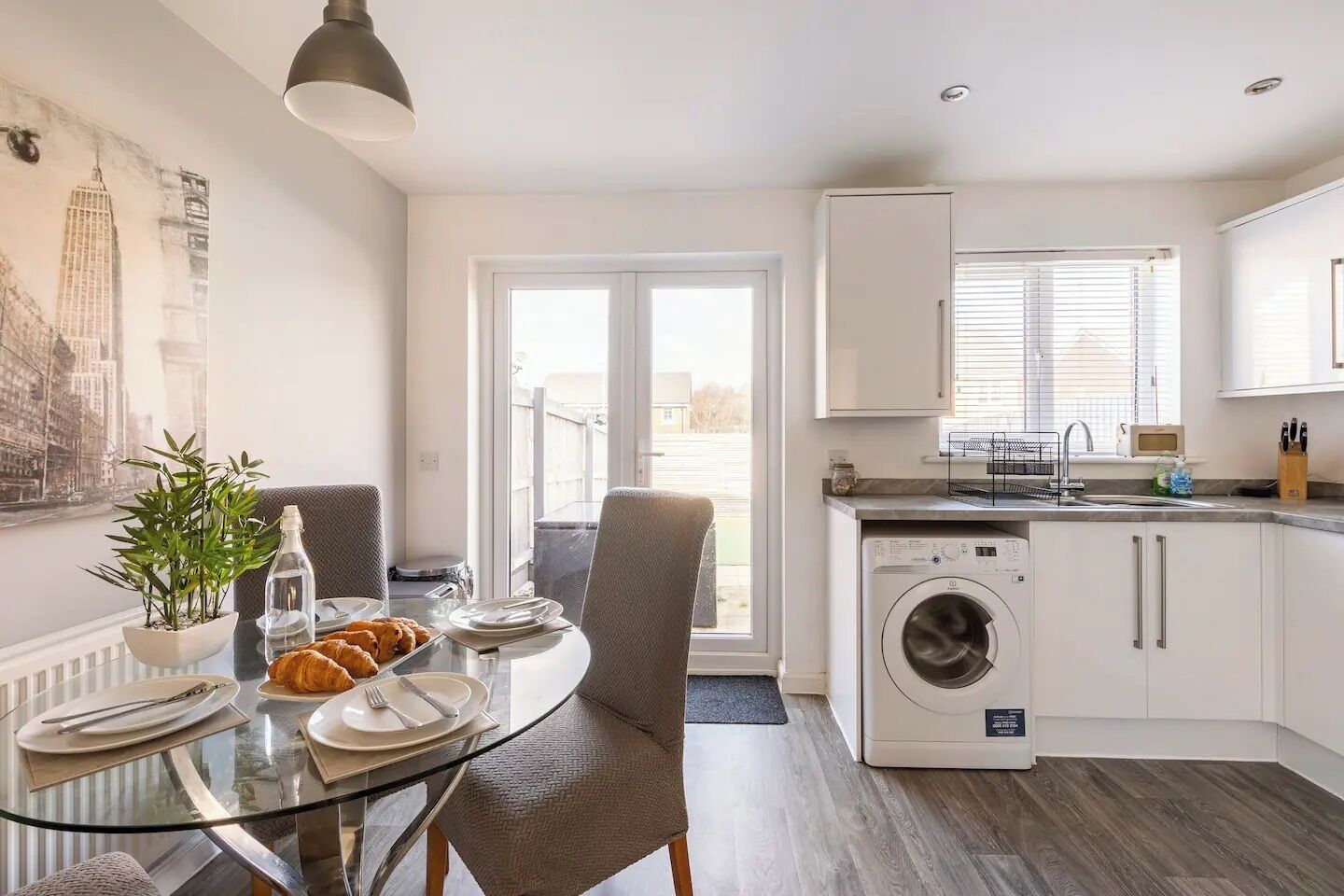 A modern kitchen with a washing machine, dining table with chairs, and a large window.