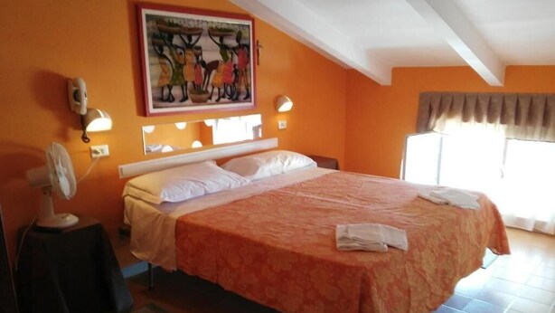 Un dormitorio con una cama, un cuadro en la pared, una lámpara de noche y una ventana con cortinas.