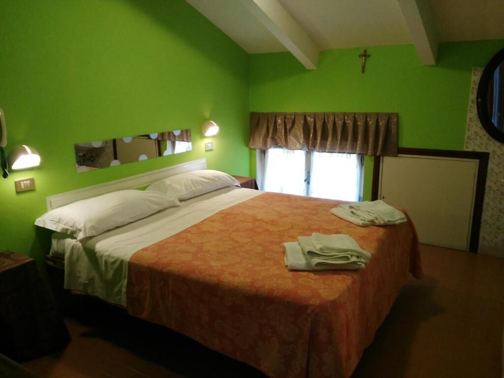 A room with a bed, a nightstand, a mirror, and a window with curtains.