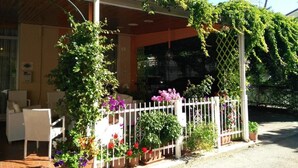 Un espacio de estar al aire libre cubierto, con plantas en macetas y una valla blanca.