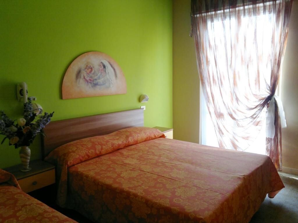 A hotel room with a bed, a nightstand, a vase with flowers, and a painting on the wall.