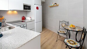 Een moderne keuken met witte kastjes, een magnetron, een rode koelkast, een spoelbak en een klein zithoekje met een tafel en stoelen.
