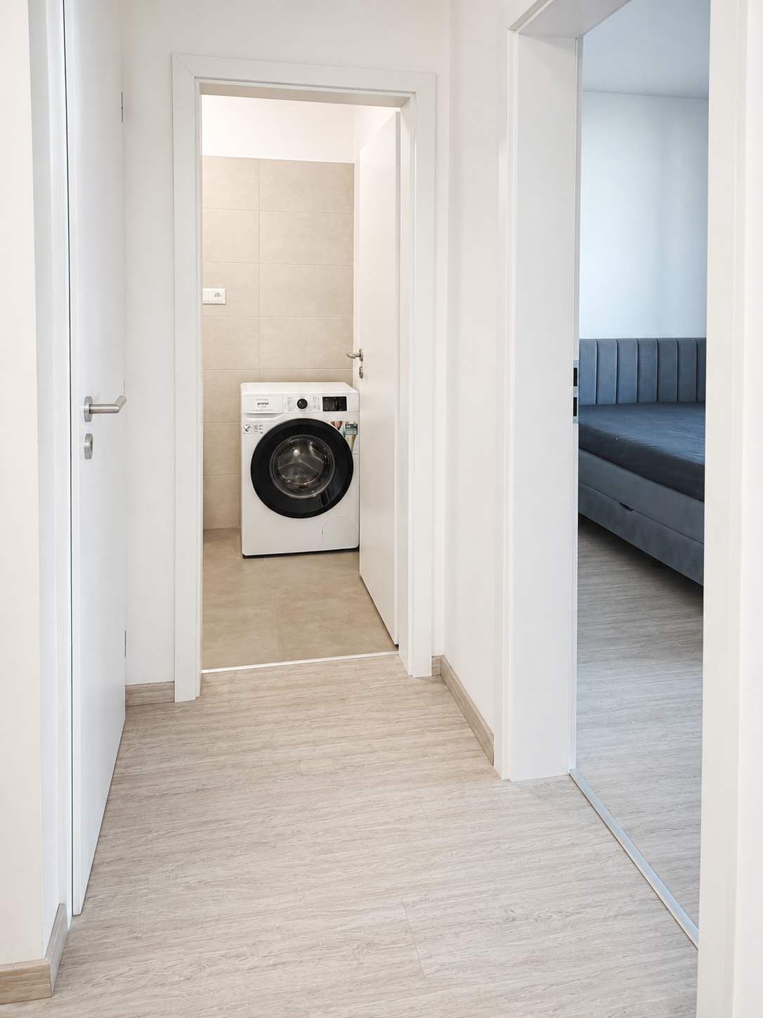 A laundry room with a washing machine, a door leading to a living area with a sofa.