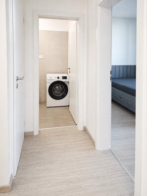 A laundry room with a washing machine, a door leading to a living area with a sofa.