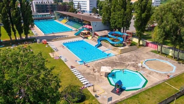 Amplia zona de piscina al aire libre con múltiples piscinas, un tobogán acuático y una zona de juegos para niños.