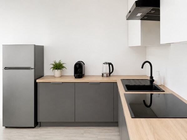 A modern kitchen with a built-in refrigerator, a coffee maker, a kettle, and a sink with a black faucet.