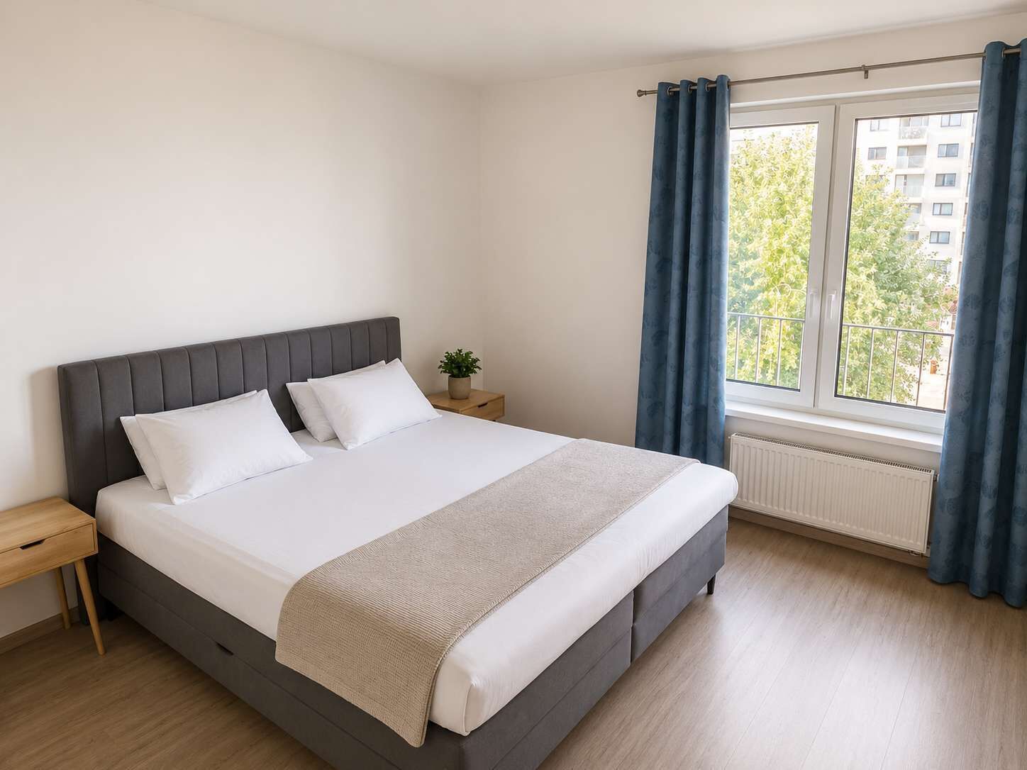 A bedroom with a bed, a nightstand, a potted plant, a window with curtains, and a radiator.