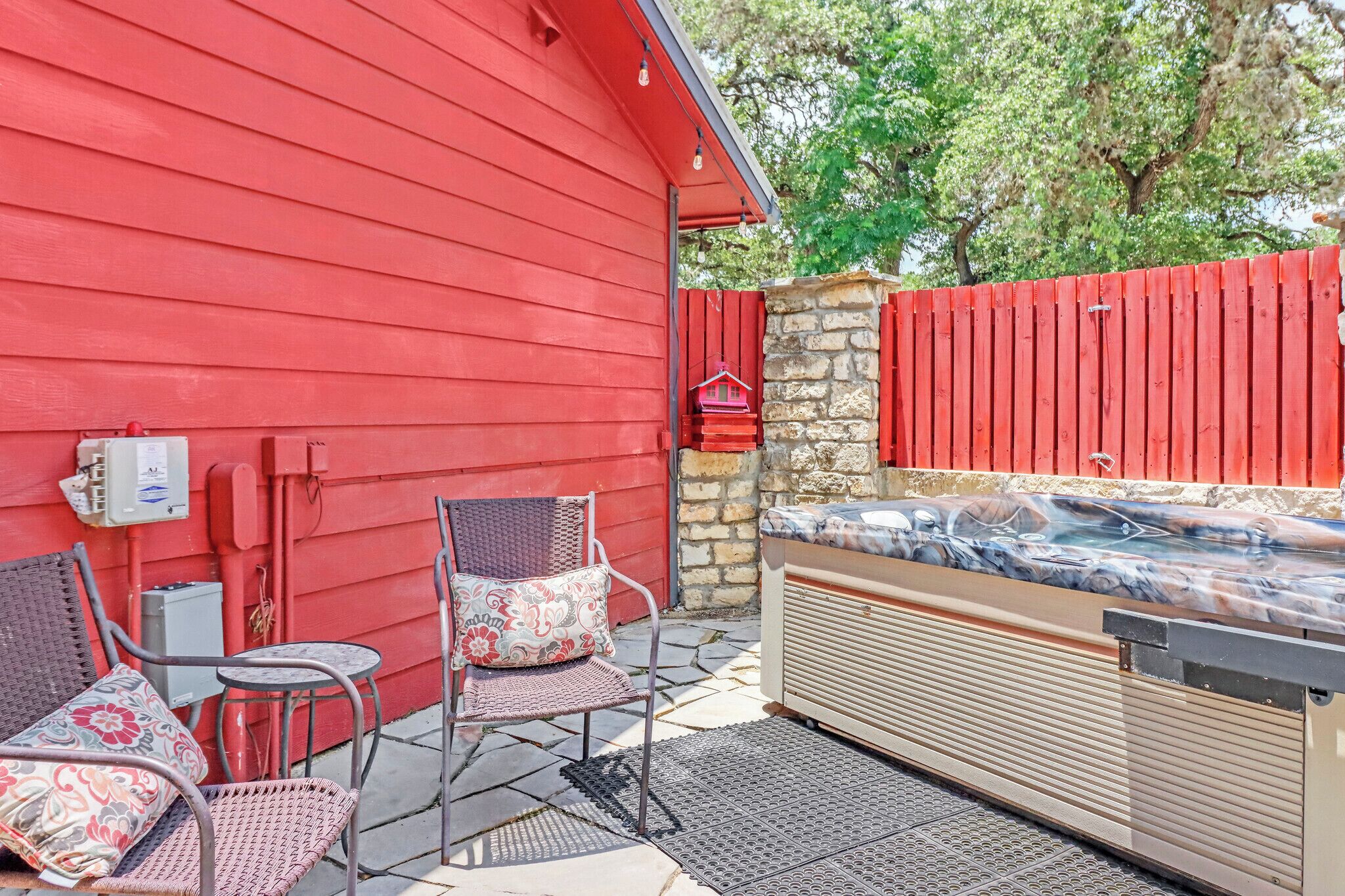 Une terrasse extérieure avec un bâtiment rouge, un mur en pierre et un barbecue.