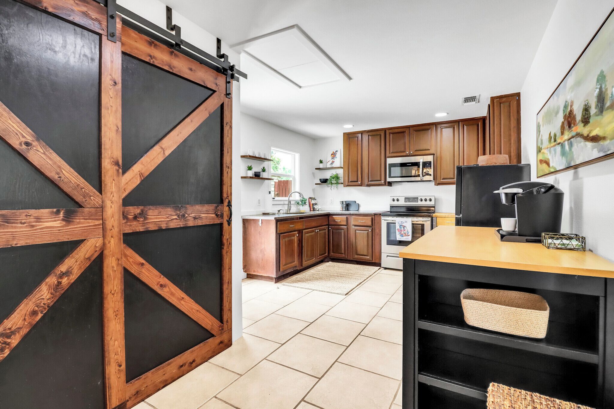 Une cuisine avec des meubles de rangement en bois, un réfrigérateur noir et une porte coulissante de style grange.
