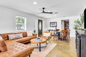 A modern living room with a leather sofa, a round coffee table, and a dining area with wooden chairs. - Wimberley Firehouse | Private Hot Tub Near Wimberley Square (Wimberley)