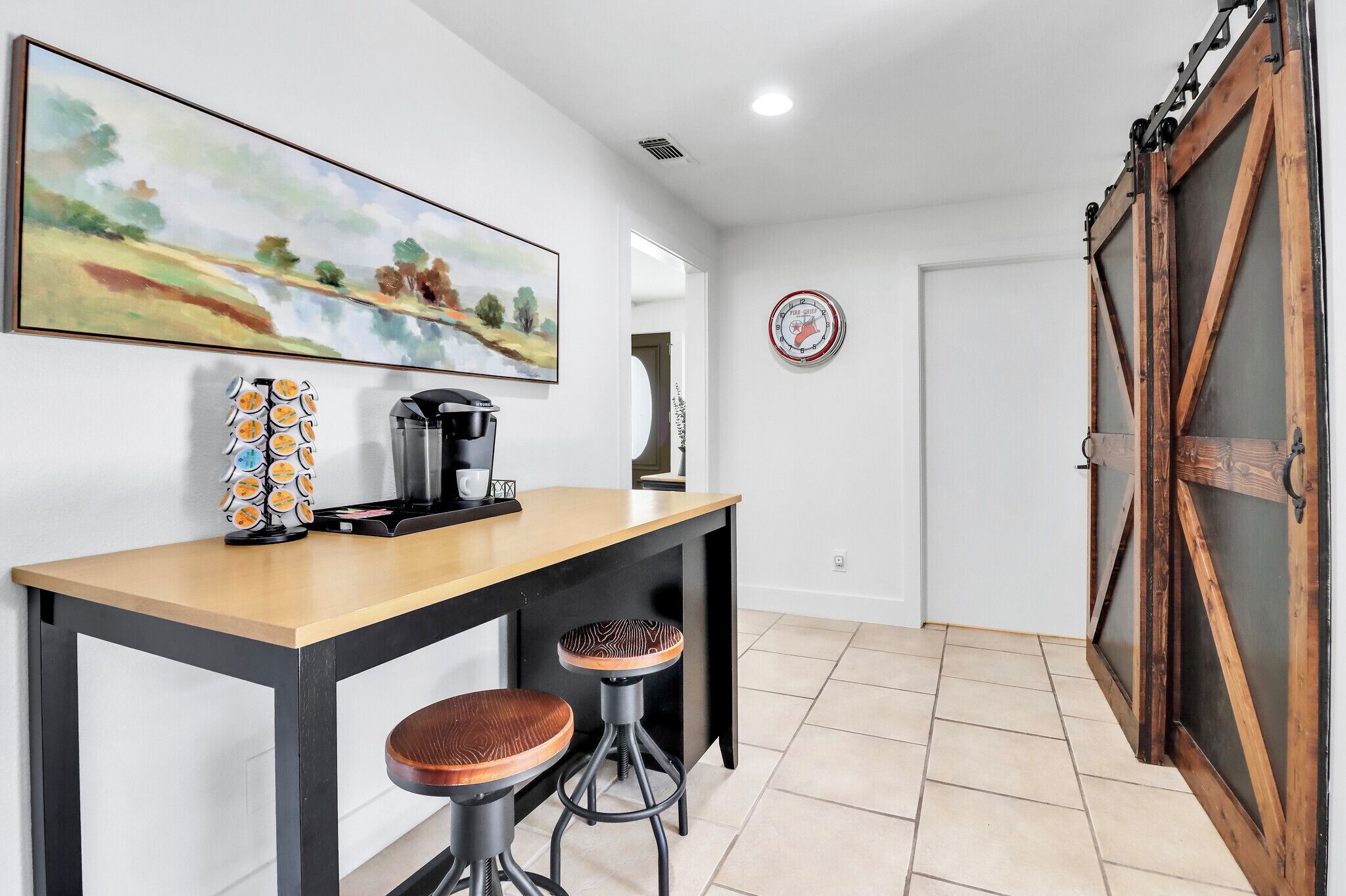 Une cuisine moderne équipée d’une machine à café, de tabourets de bar et d’un tableau accroché au mur.