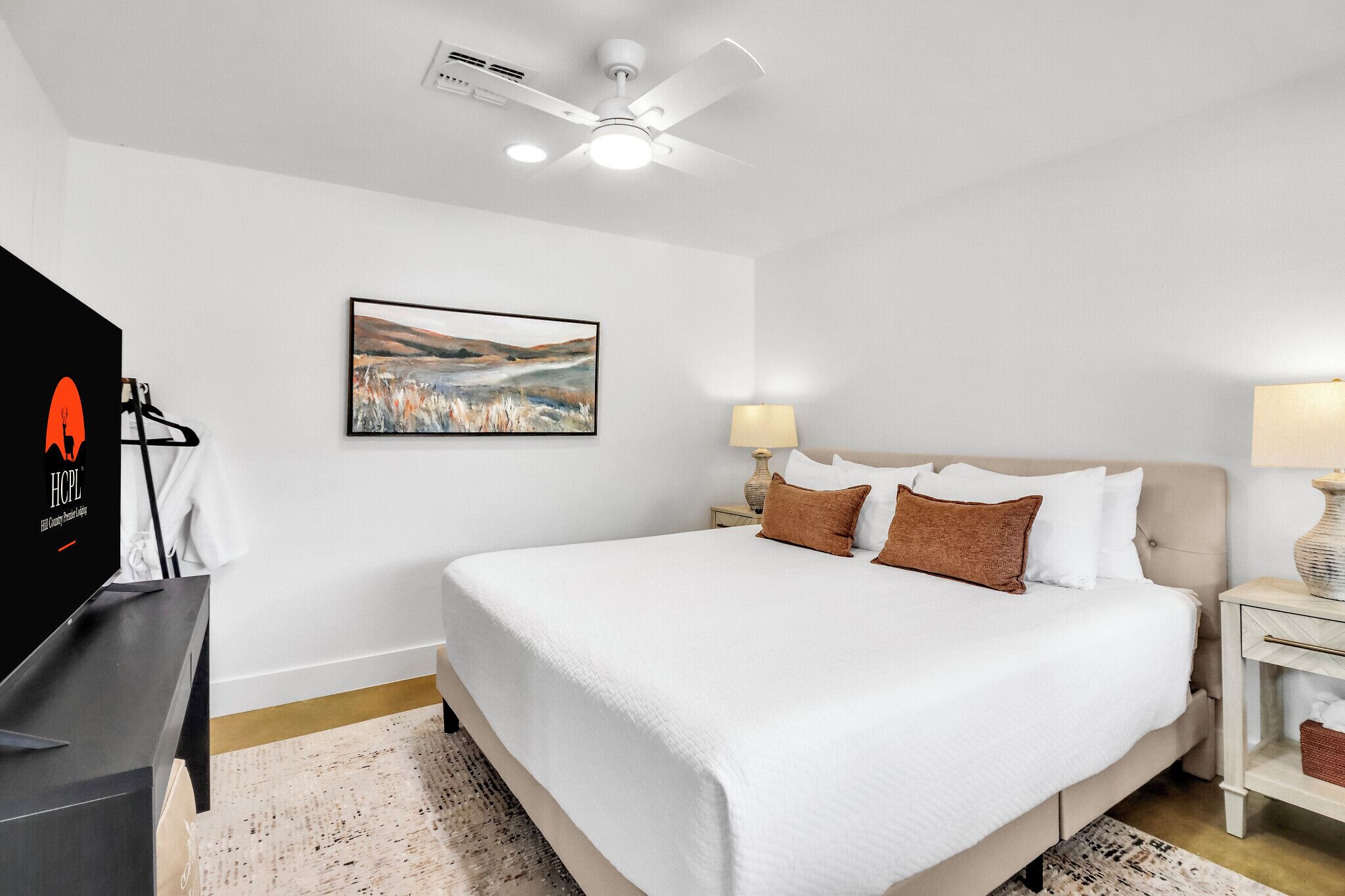 Une chambre d’hôtel avec un lit, un ventilateur de plafond, un tableau, une télévision et une lampe.
