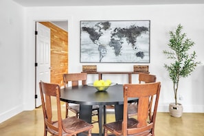 A dining area with a round table, six wooden chairs, a world map on the wall, a potted plant, and a basket on the table. - Wimberley Firehouse | Private Hot Tub Near Wimberley Square (Wimberley)