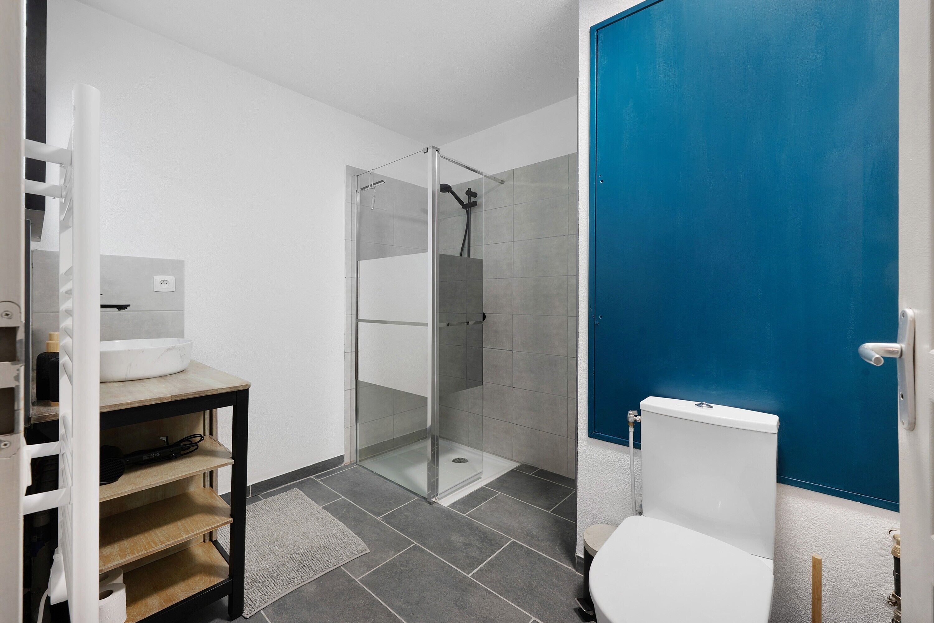 Um banheiro moderno com box de vidro, vaso sanitário branco e porta azul.