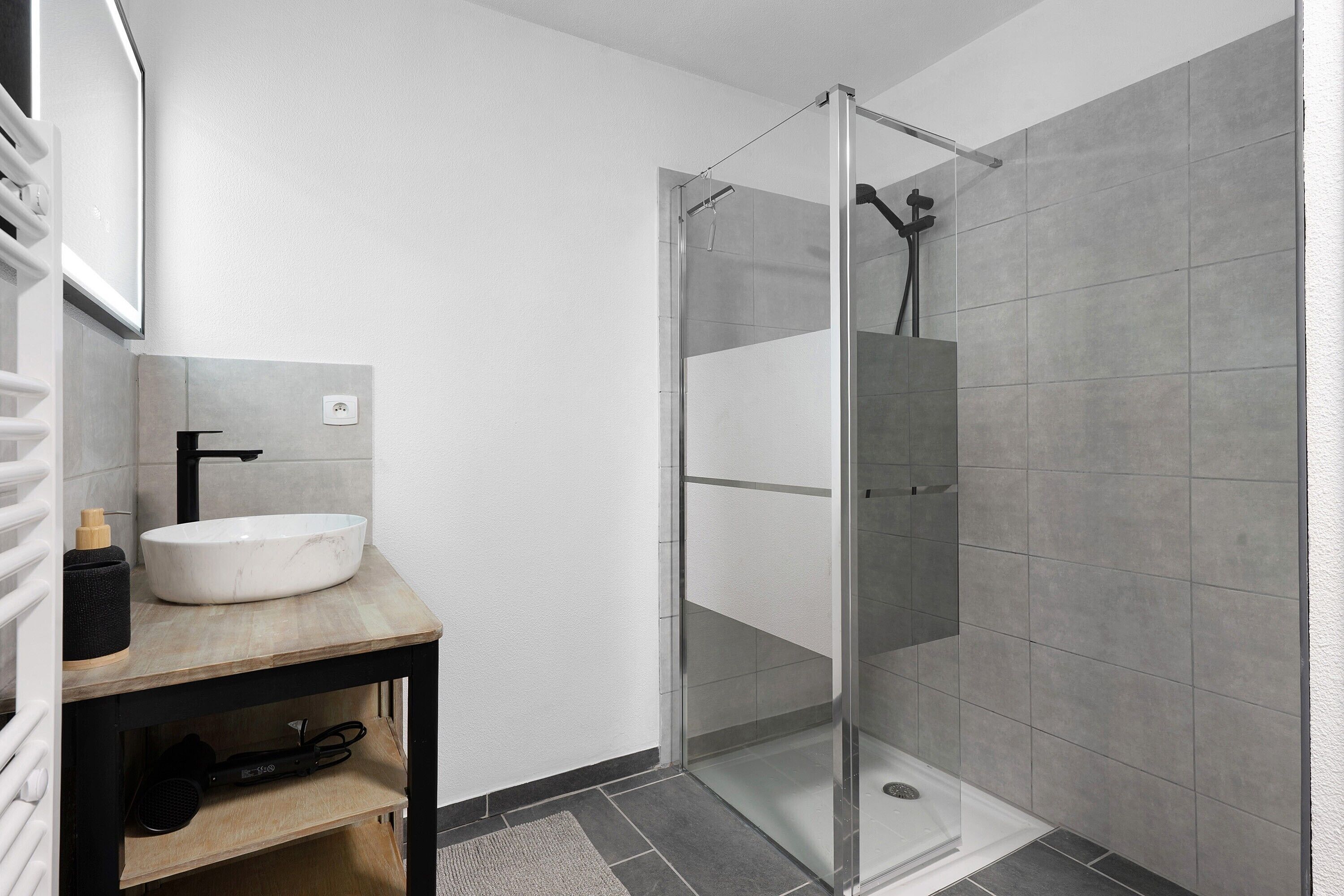 Une salle de bain moderne avec une douche à parois de verre, un lavabo blanc et un meuble-lavabo en bois.