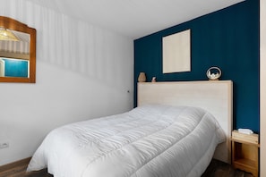 Een slaapkamer met een bed, een spiegel, een wandlamp en een klein plankje met decoratieve objecten.