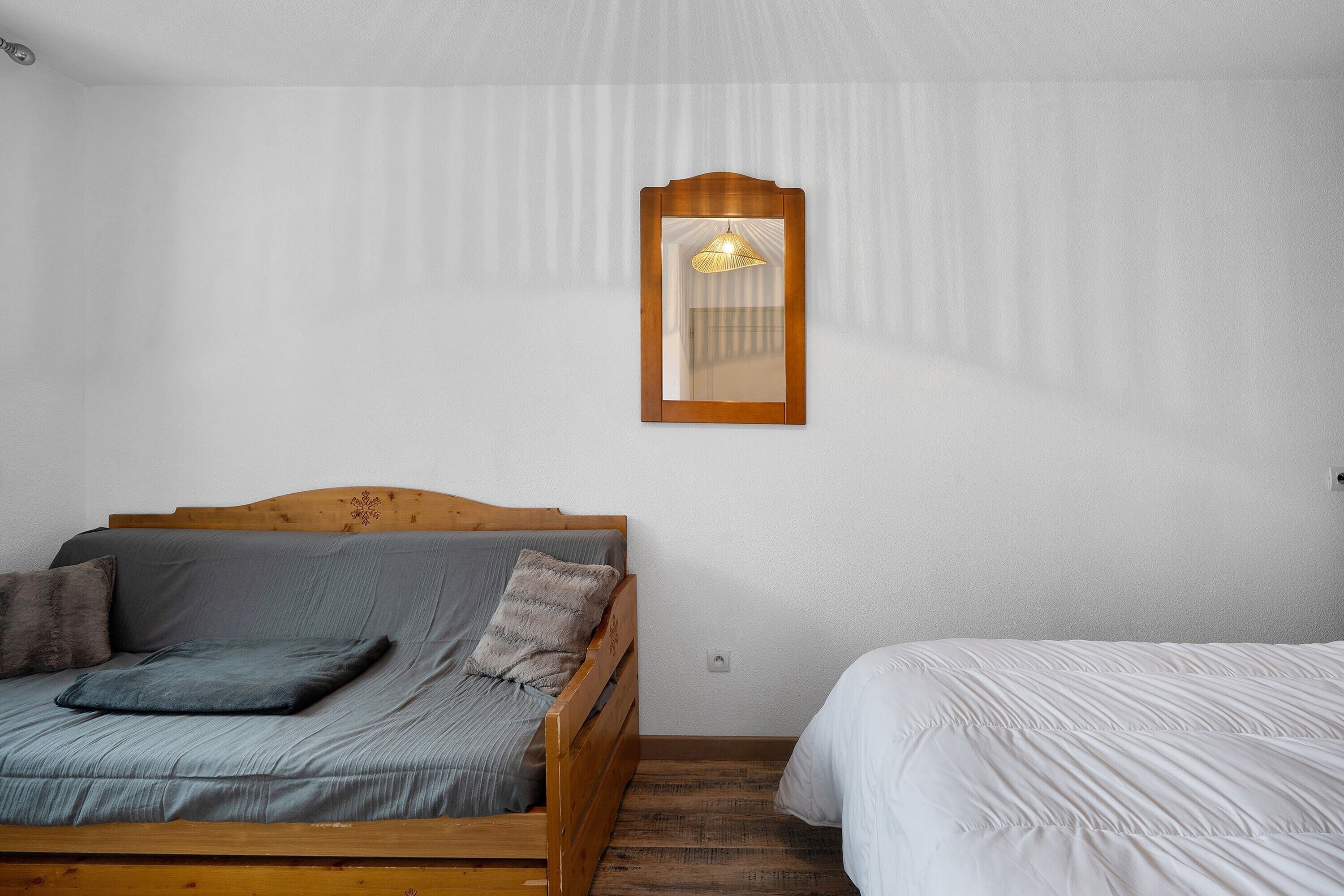 Une chambre avec un lit en bois, une petite table de chevet et un miroir fixé au mur.