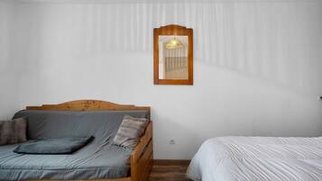 Une chambre avec un lit en bois, une petite table de chevet et un miroir fixé au mur.