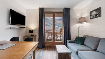 Een kamer met televisie, een tafel, een bank, een lamp en uitzicht op bergen door een deur.