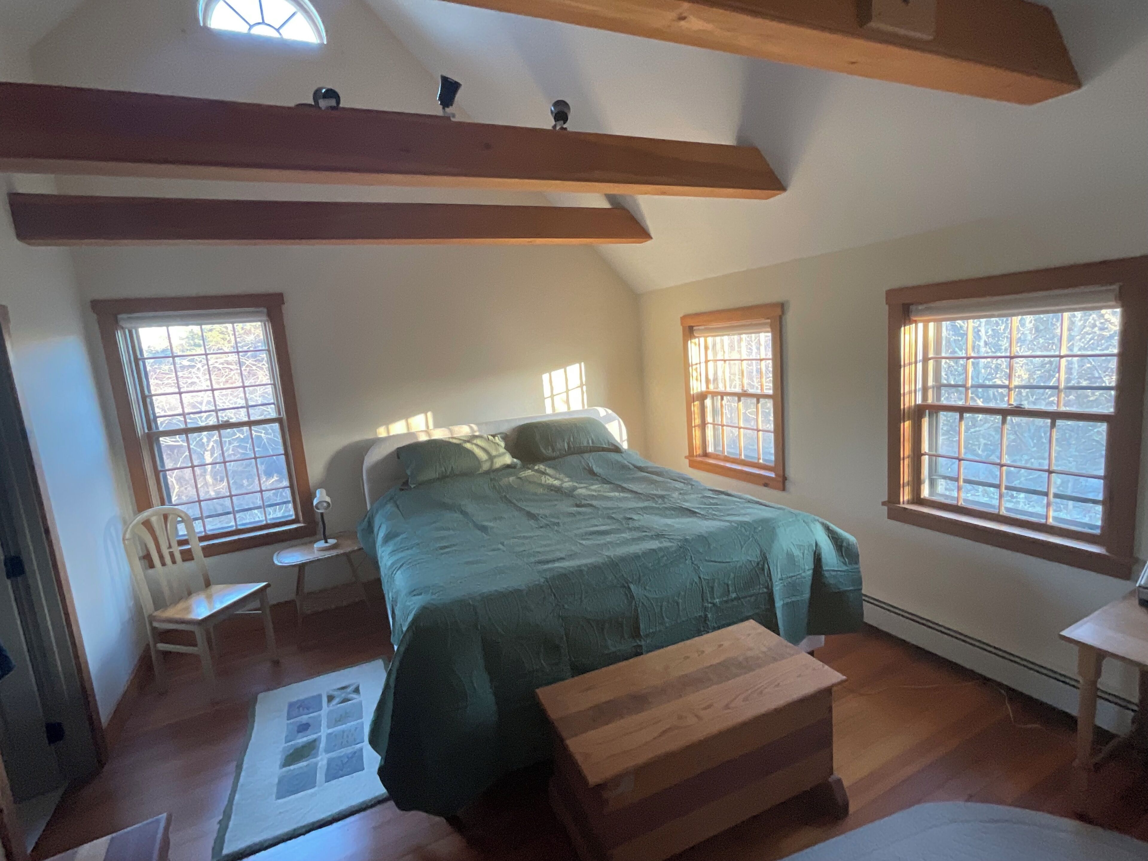 A bedroom with a bed, a wooden bench, a chair, and two windows.