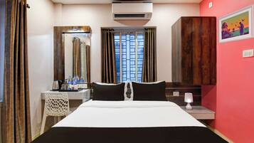 Habitación de hotel con cama, escritorio con espejo, aire acondicionado, ventana con cortinas y una pared con un cuadro enmarcado.
