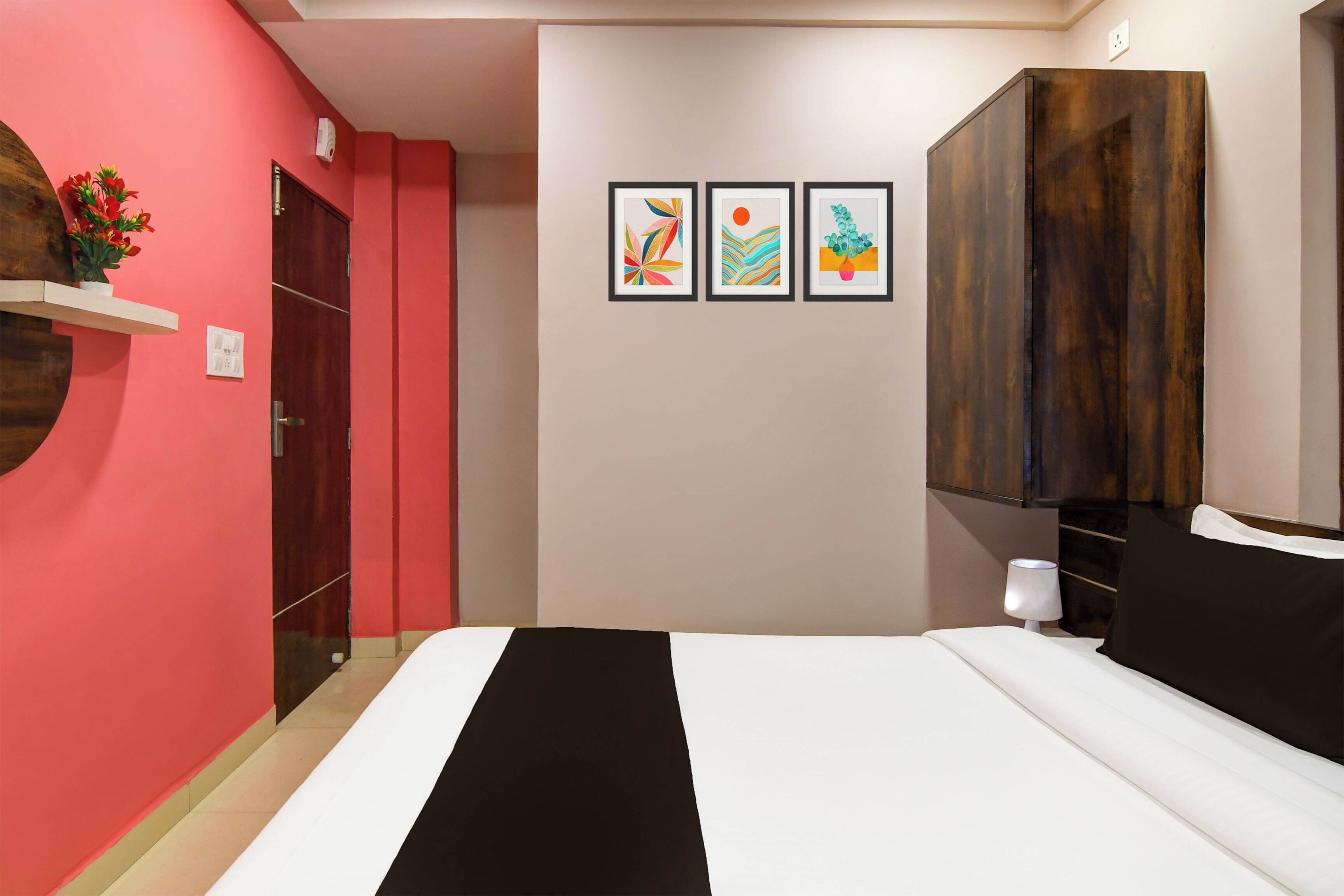 Un dormitorio con una cama, un armario, un estante de pared con una planta en maceta y tres cuadros enmarcados.