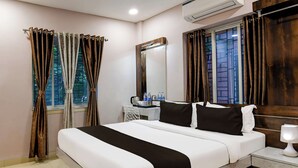 Una habitación de hotel con cama, mesita de noche, espejo, ventana con cortinas y un equipo de aire acondicionado.